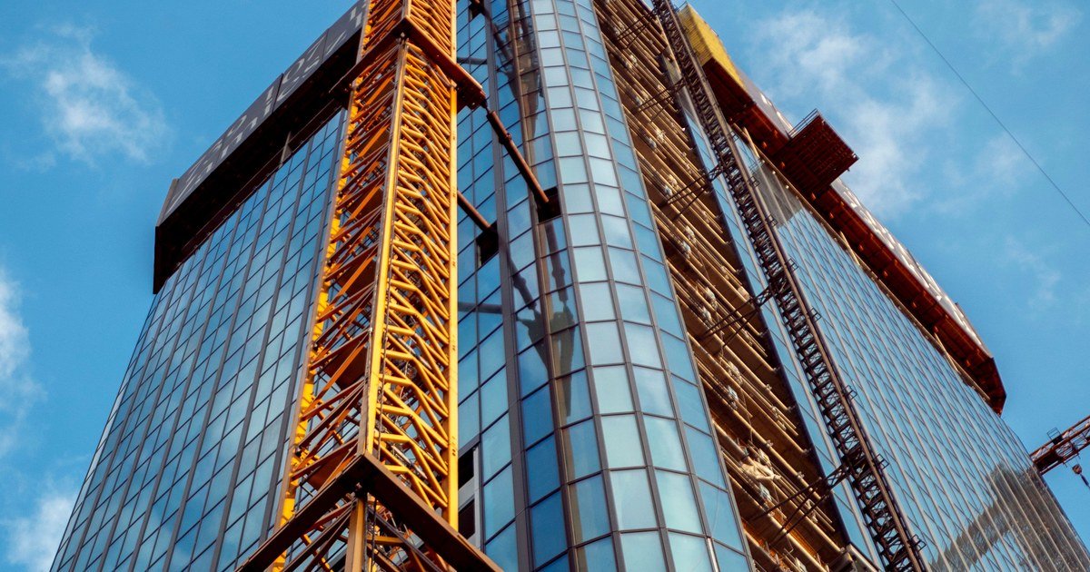 Tòa nhà cao tầng mặt kính đang thi công với cần cẩu xây dựng, chụp từ dưới nhìn lên