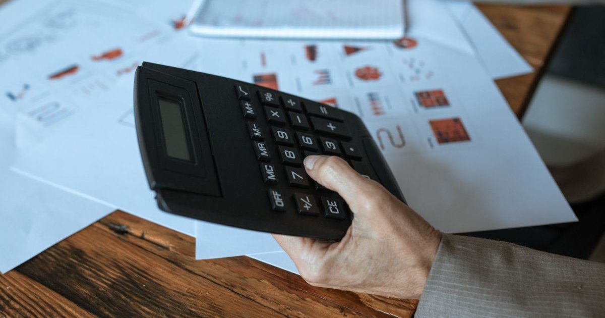 Bàn tay cầm máy tính trên nền tài liệu biểu đồ