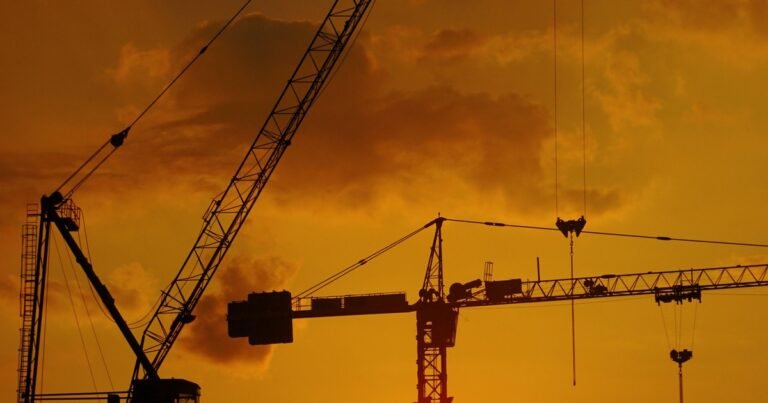 Cần trục tháp trên công trường xây dựng in bóng dưới ánh hoàng hôn