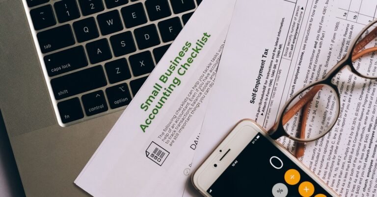 Tài liệu checklist kế toán, thuế đặt cạnh bàn phím máy tính, kính mắt và điện thoại hiển thị máy tính