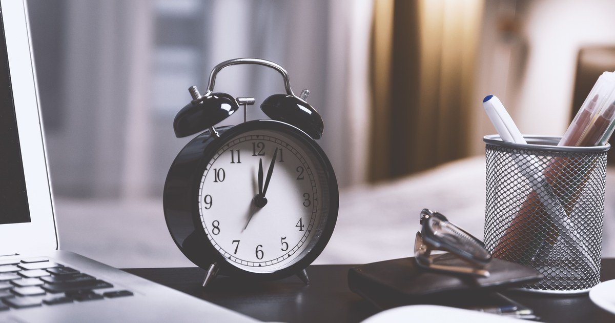 Overtime Limits: 40 Hours/Month, 200 or 300 Hours/Year? 1 Đồng hồ báo thức trên bàn làm việc cạnh laptop, minh họa quy định giới hạn giờ làm thêm của người lao động