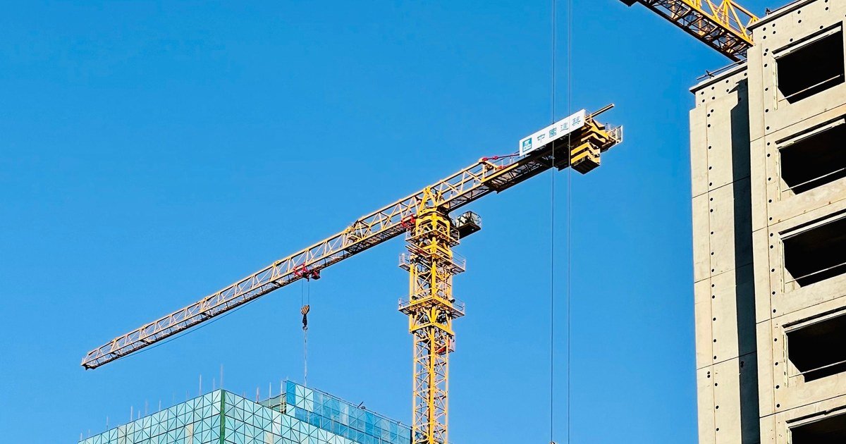 Cần cẩu tháp màu vàng tại công trường xây dựng tòa nhà cao tầng dưới trời xanh