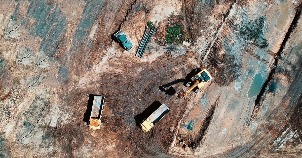 补偿、征地拆迁与土地使用者的权利 1 Công trường giải phóng mặt bằng nhìn từ trên cao với máy xúc và xe tải, minh họa chính sách đền bù đất đai