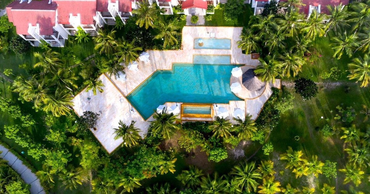 Resort Project Transfer Blocked by Planning: Case Study 1 Toàn cảnh khu nghỉ dưỡng nhiệt đới nhìn từ trên cao với hồ bơi và hàng dừa xanh