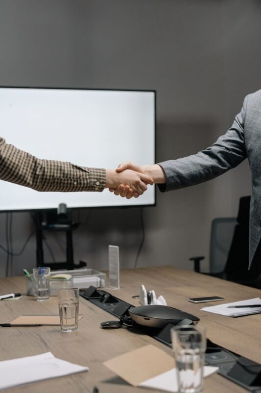 Two professionals shaking hands in a modern meeting room — illustrating a settlement reached through commercial mediation