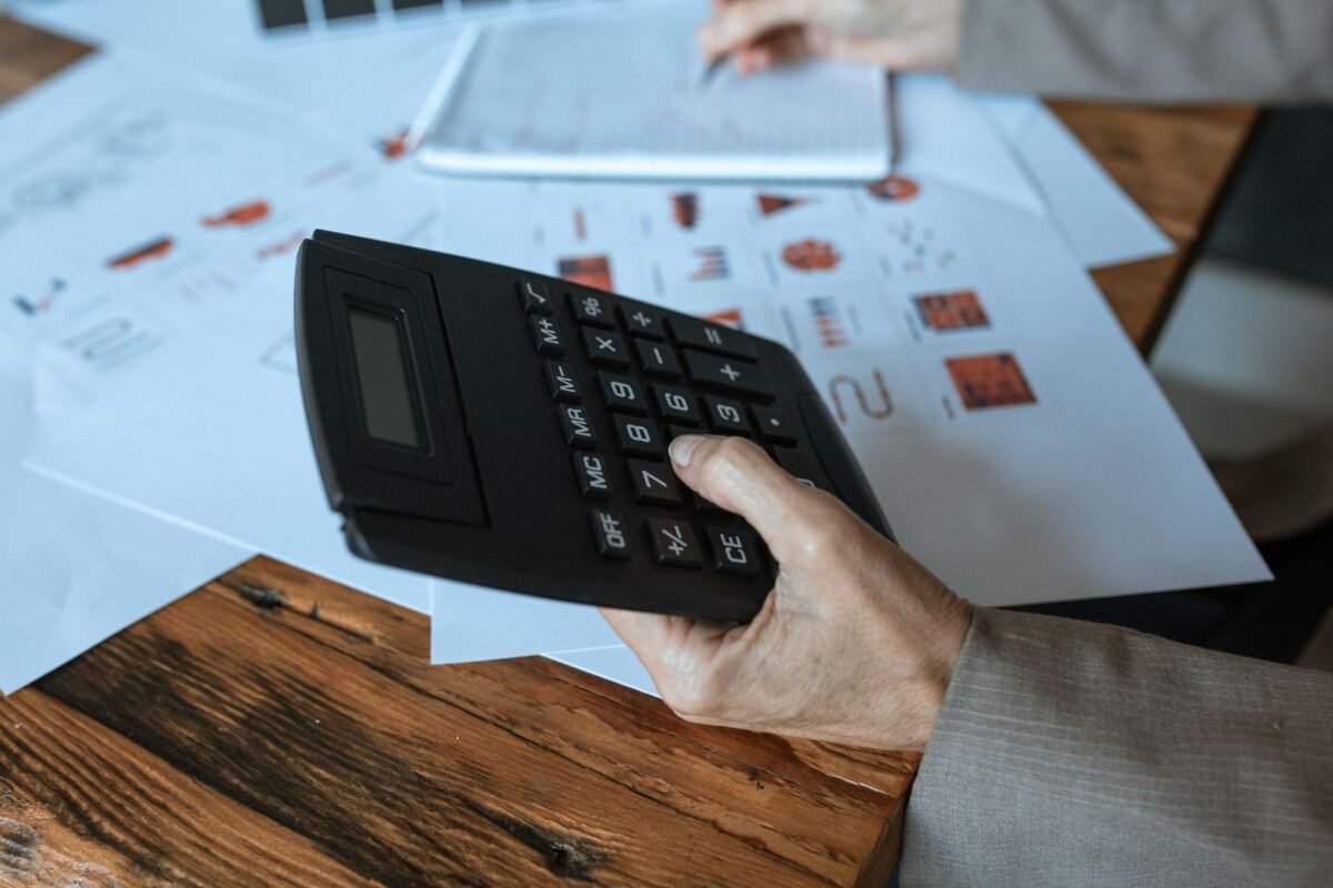 Hand using a calculator over financial documents — illustrating annual CIT finalization, no face visible