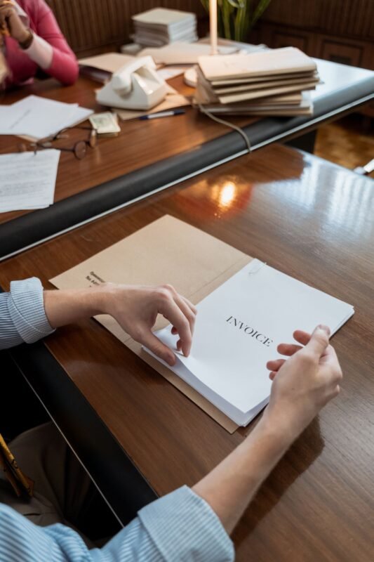 Bàn tay cầm tập hóa đơn có chữ INVOICE trên bàn làm việc gỗ — minh họa bài viết về hóa đơn điện tử có mã và không có mã của cơ quan thuế