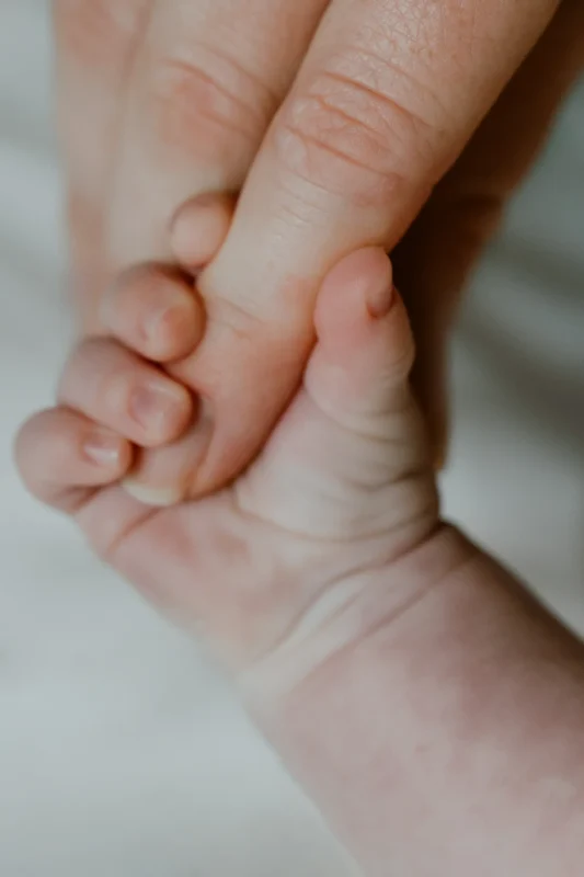 Newborn baby grasping mothers finger; faces not shown
