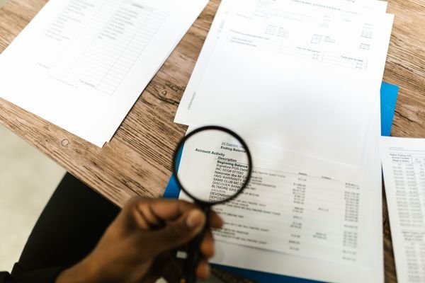 Hand holding a magnifying glass over bank audit documents — illustrating corporate duties to report suspicious transactions under AML rules