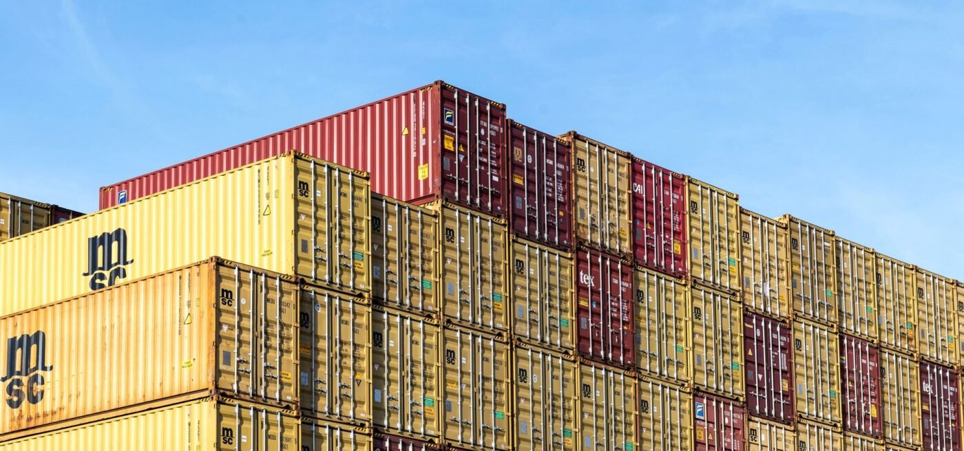 Stacked shipping containers at a freight terminal — temporary import for re-export concept, no people visible
