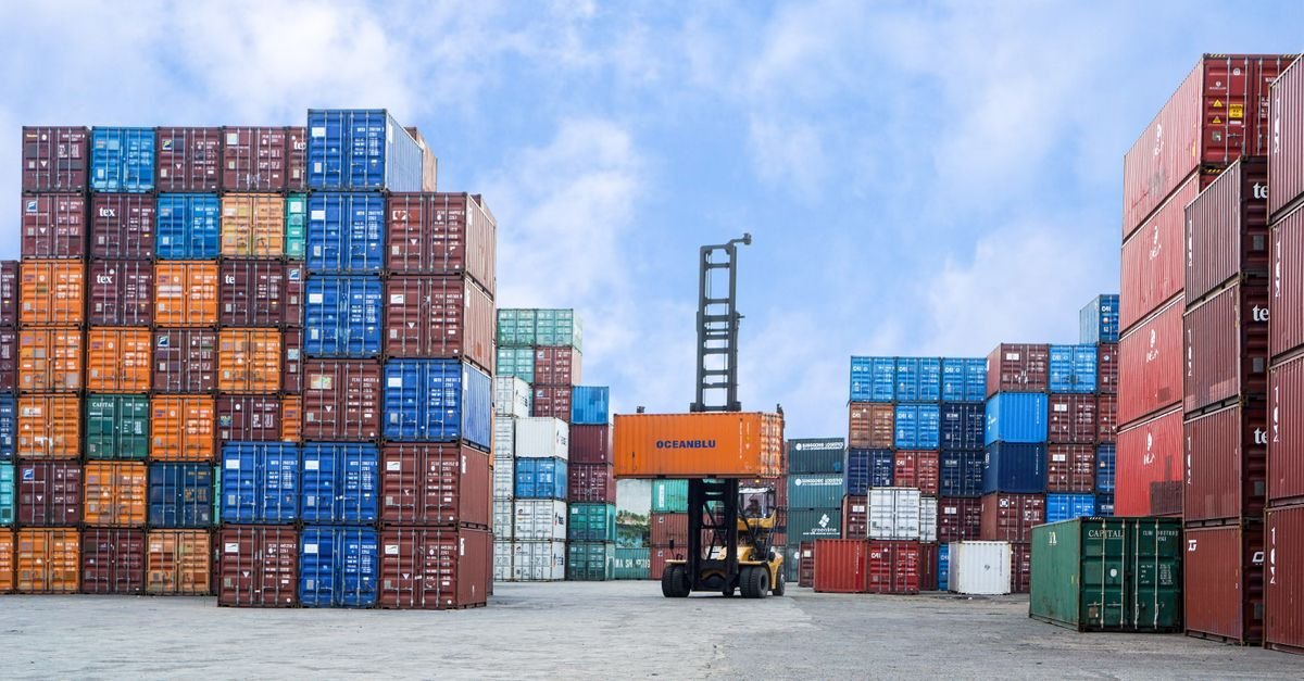 Xe nâng di chuyển container tại bãi cảng — minh họa tạm nhập tái xuất hàng hóa, không mặt người