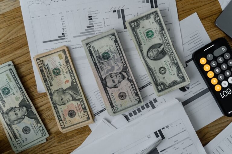 US dollar bills, financial documents and calculator on wooden desk