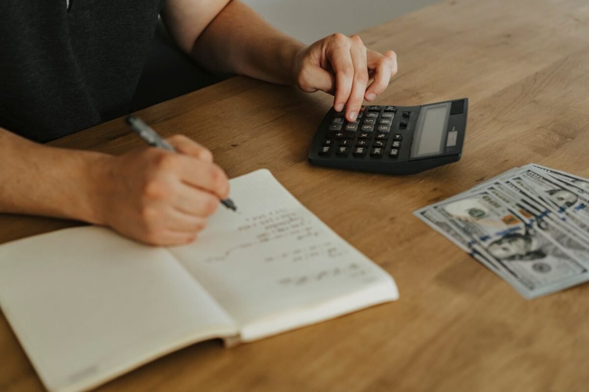 Hands using calculator and writing in notebook with cash on desk