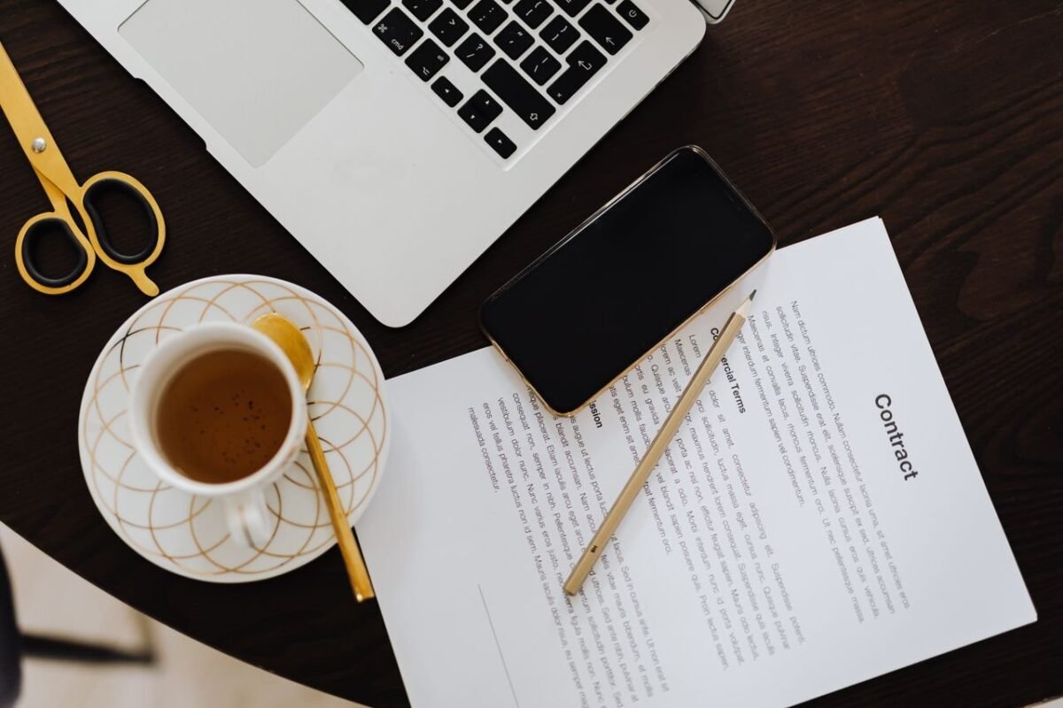Contract documents on a desk with laptop and phone — illustrating an article on registering trademark licence contracts at the IP Office