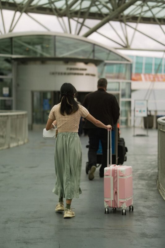 Woman in Brown T Shirt Pushing Her Pink Luggage and Man in Black Long Sleeves Pushing Trolley