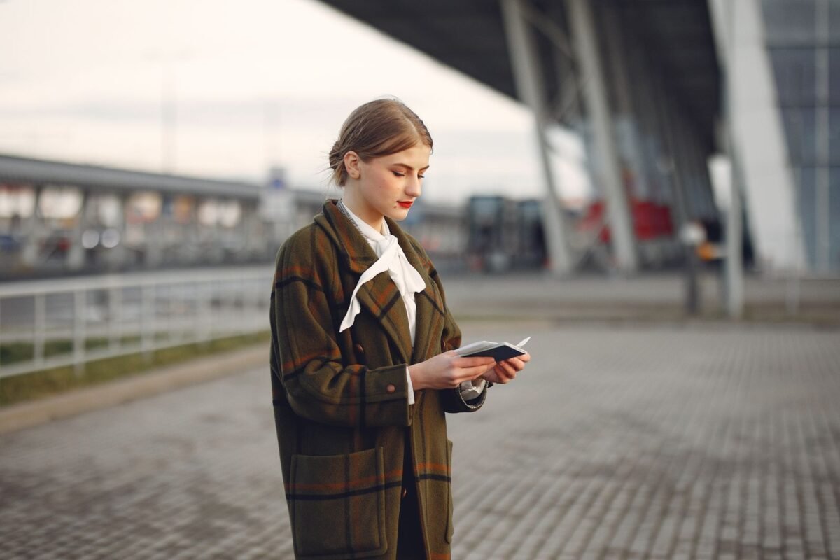 Young confident woman reading documents while standing near airport terminal