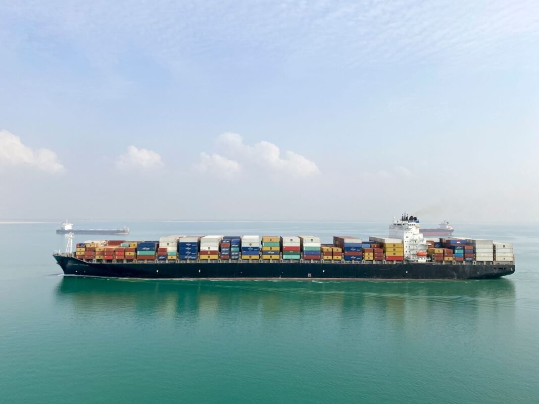 Aerial view of a large cargo ship filled with containers sailing on a calm sea under a clear sky