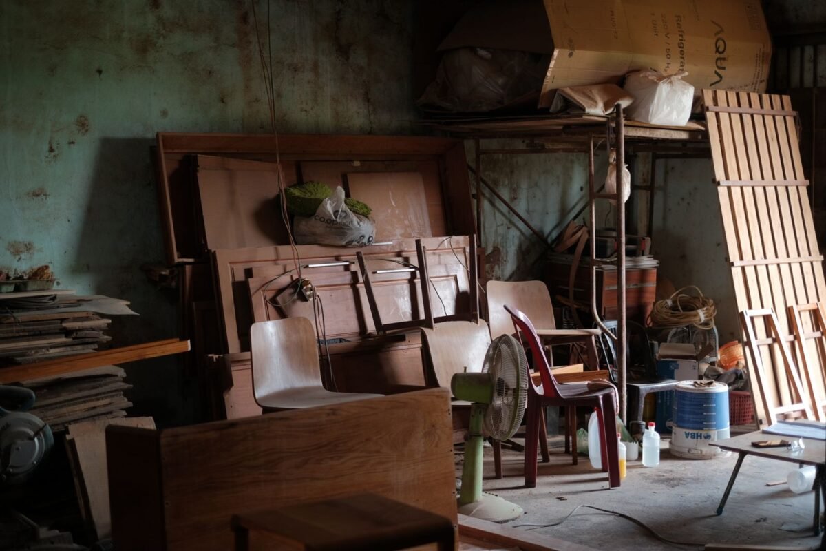 A cluttered workshop filled with wooden furniture, tools, and various items in natural lighting
