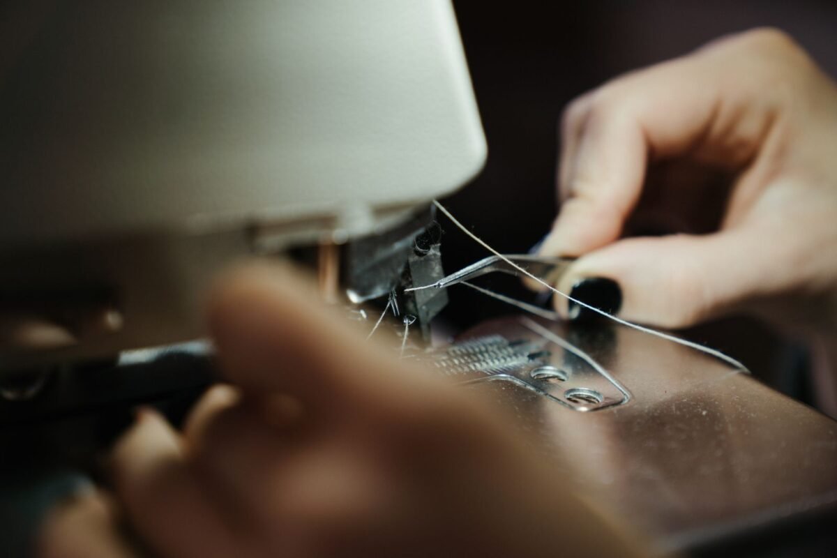 A close-up of hands threading a sewing machine in a workshop setting