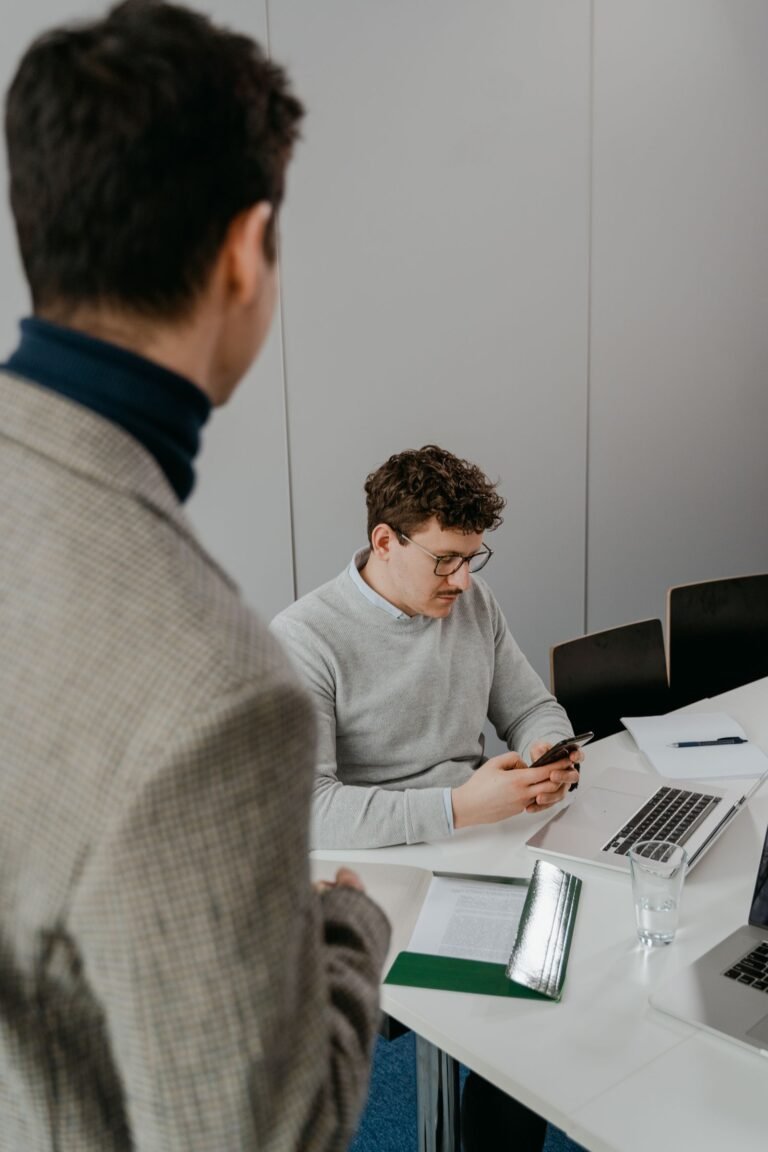 Two colleagues engage in a business meeting using laptops and smartphones in a modern office setting