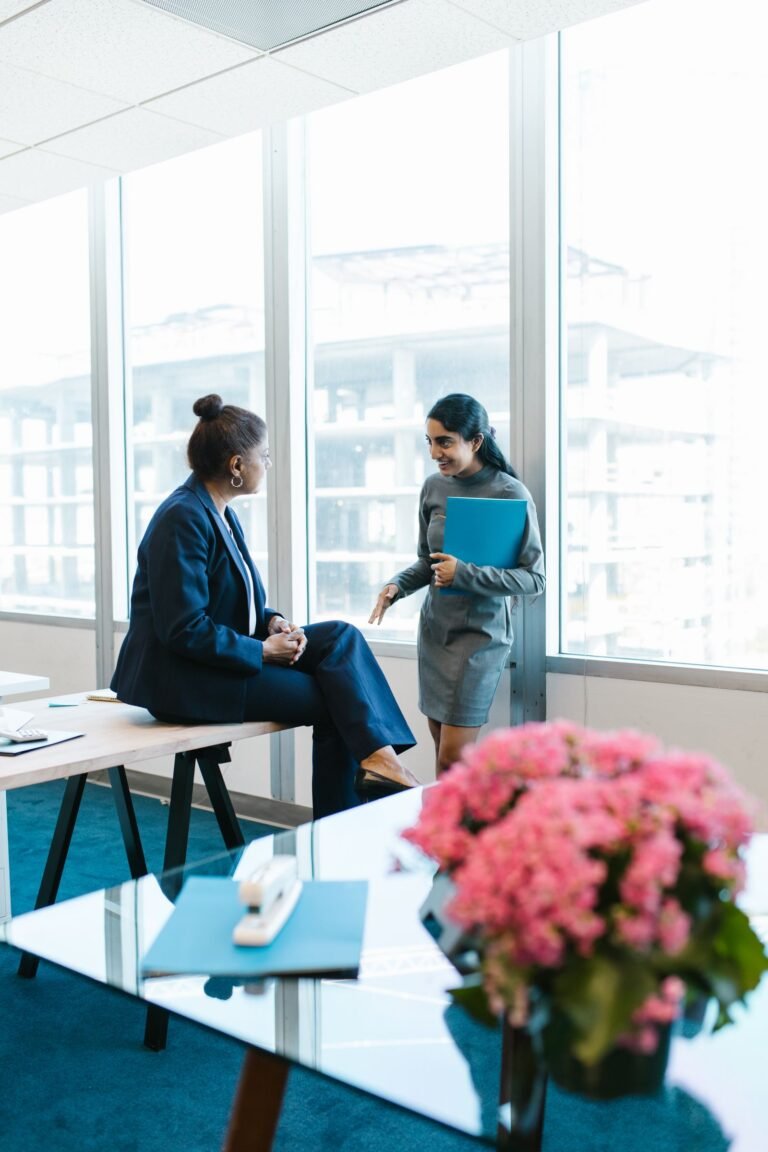 Two professional women in business attire having a conversation in a modern office setting