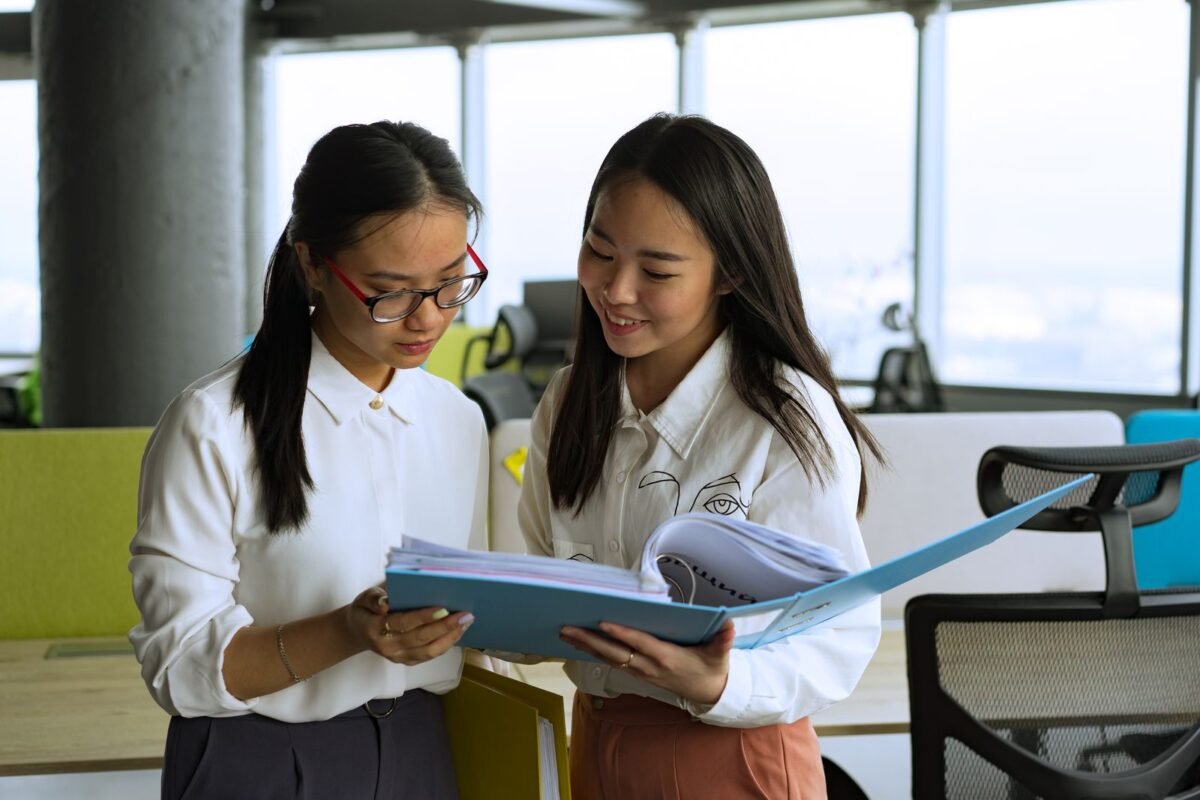 Two professional women reviewing documents together in a modern office setting, emphasizing teamwork