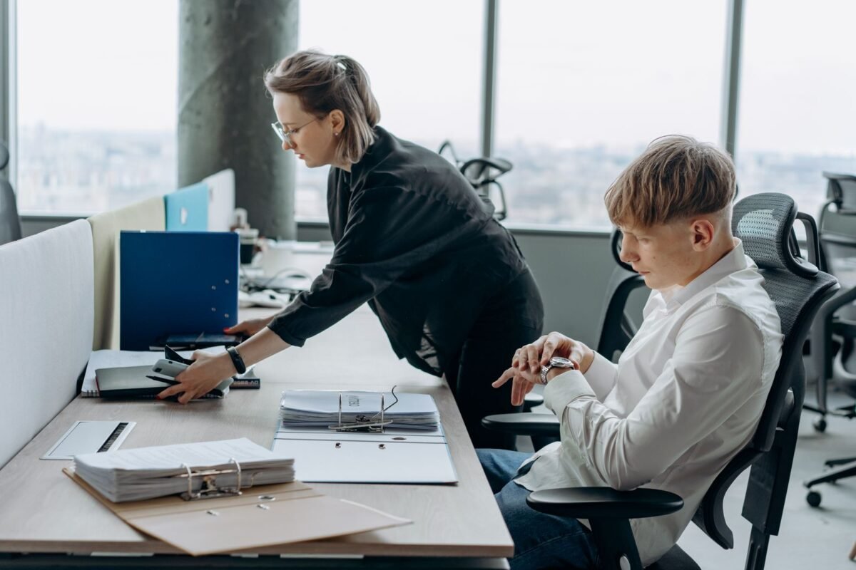 Two business professionals working together in a modern office environment with documents and computers