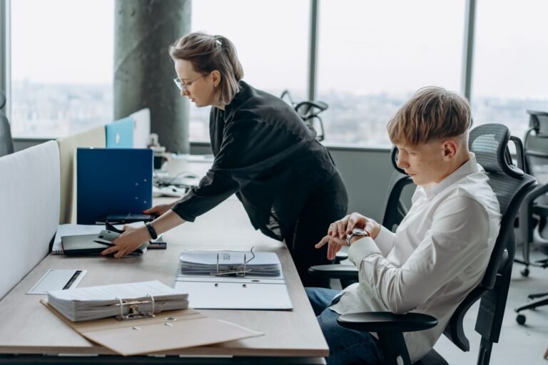 Two business professionals working together in a modern office environment with documents and computers