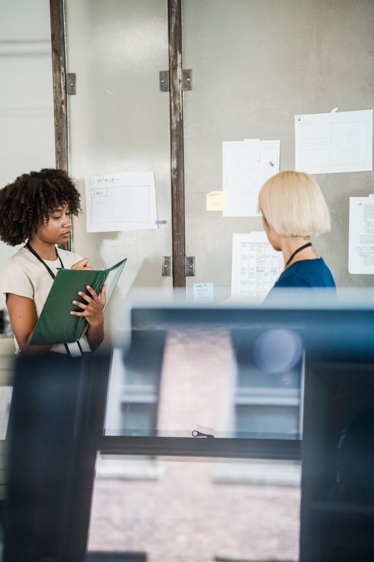 Two professional women discussing ideas in a modern office with documents on the wall