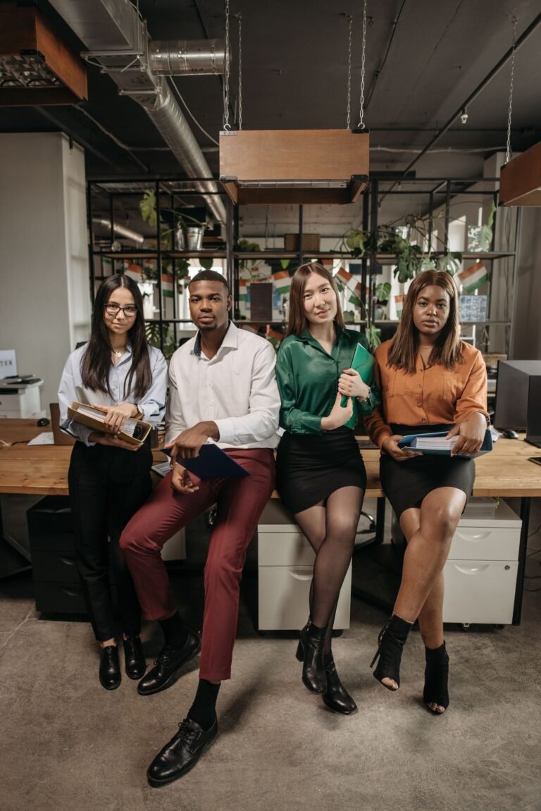 A diverse group of young professionals posing in a modern office setting, holding folders and looking confident