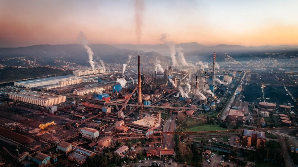Aerial view of a factory with chimneys emitting smoke during sunset