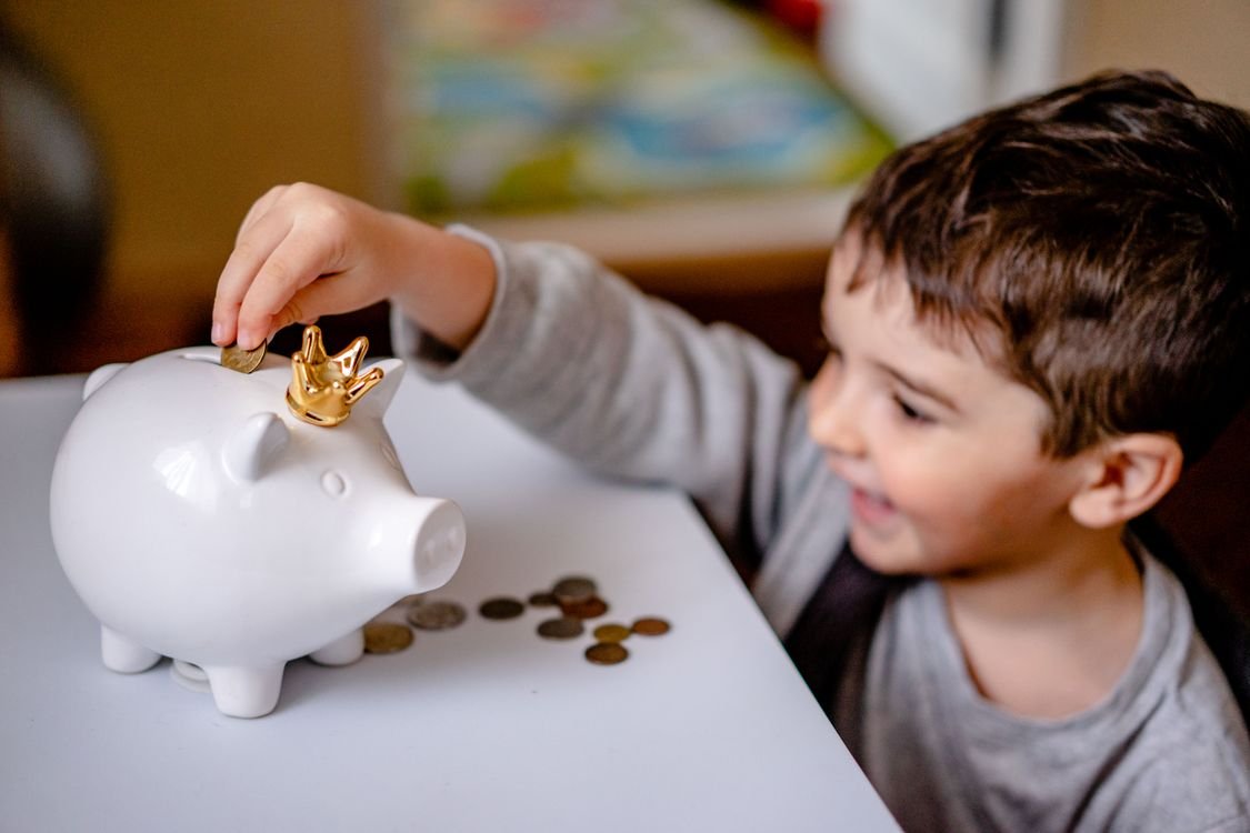 Young boy smiling while saving money in a crowned piggy bank demonstrating financial responsibility