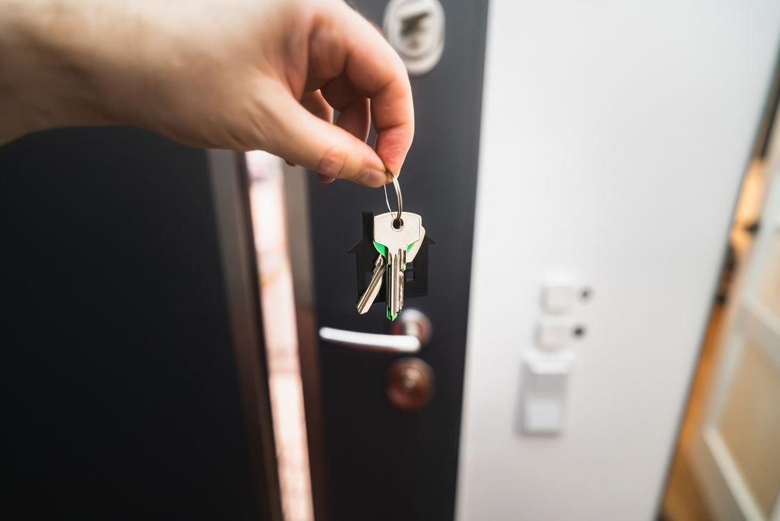Close-up of a hand holding keys in front of an open door symbolizing new homeownership