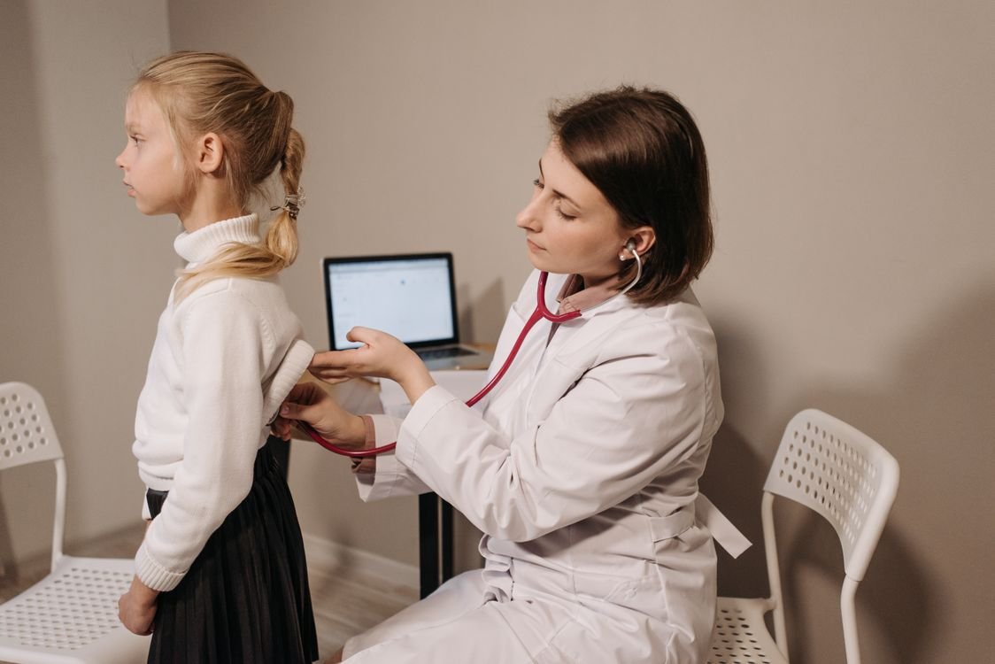 A doctor uses a stethoscope during a child medical exam in a clinic setting