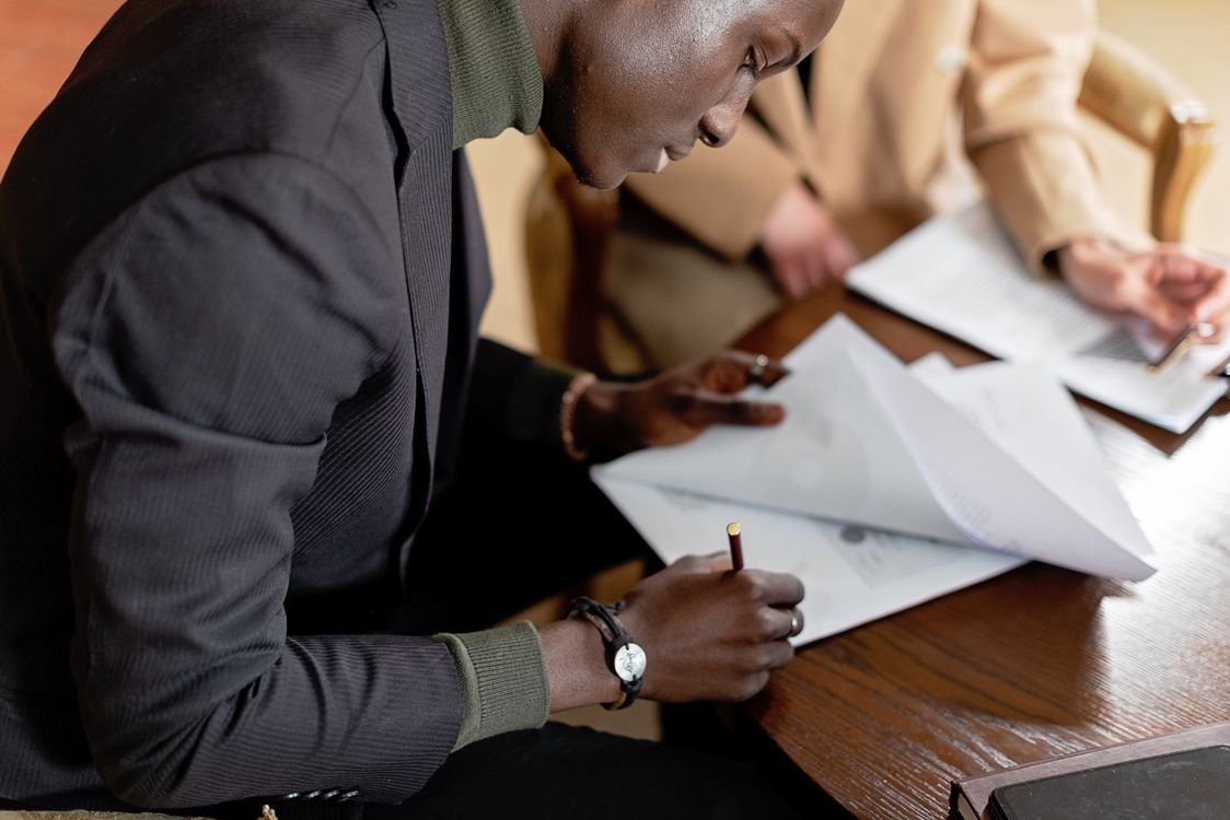 A man in a blazer signing important business documents at a desk