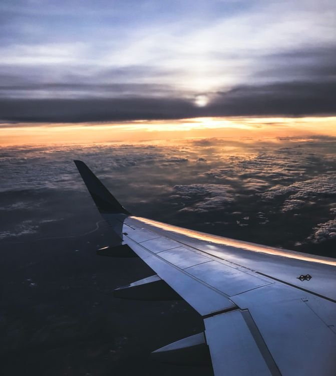 View from an airplane window showing wing and sunset over clouds