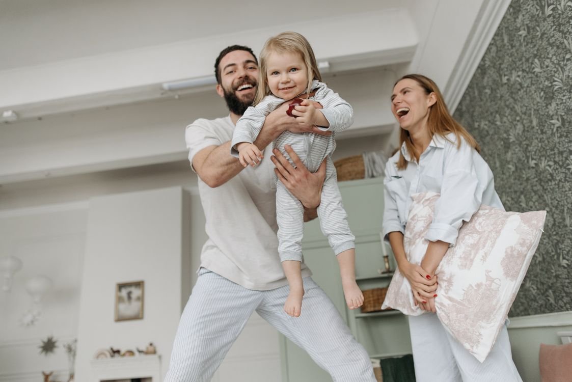 Cheerful family with parents playing and lifting child in a cozy living room