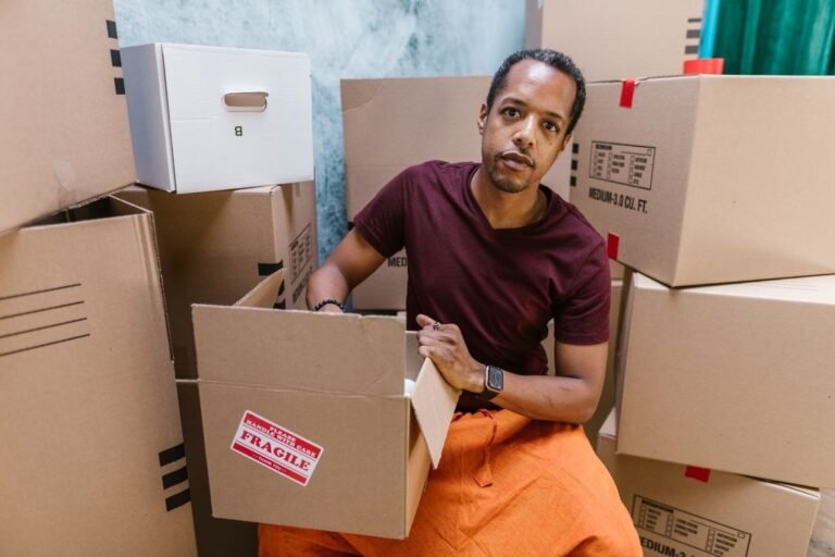 Close-Up Shot of a Man in Maroon Shirt Holding a Cardboard Box