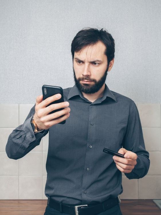Worried Man Checking Phone with Credit Card