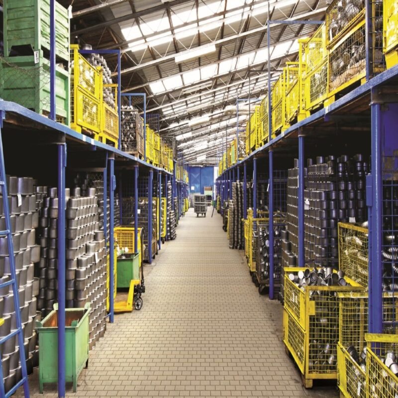 Miễn thuế nhập khẩu nguyên liệu để sản xuất hàng xuất khẩu 1 Miễn thuế nhập khẩu nguyên liệu để sản xuất hàng xuất khẩu — lối đi kho bãi với container kim loại trên kệ, không người