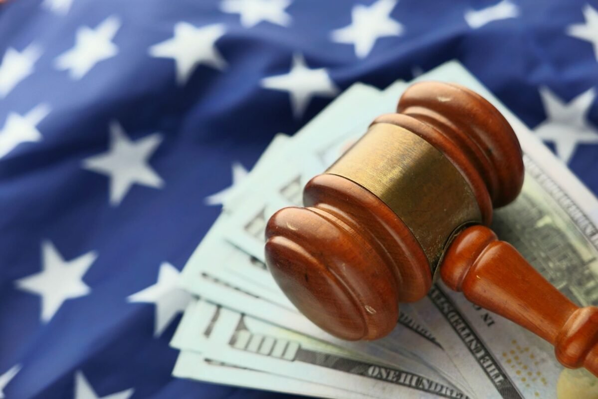Close-up of a gavel on US dollar bills with American flag backdrop symbolizing justice and finance